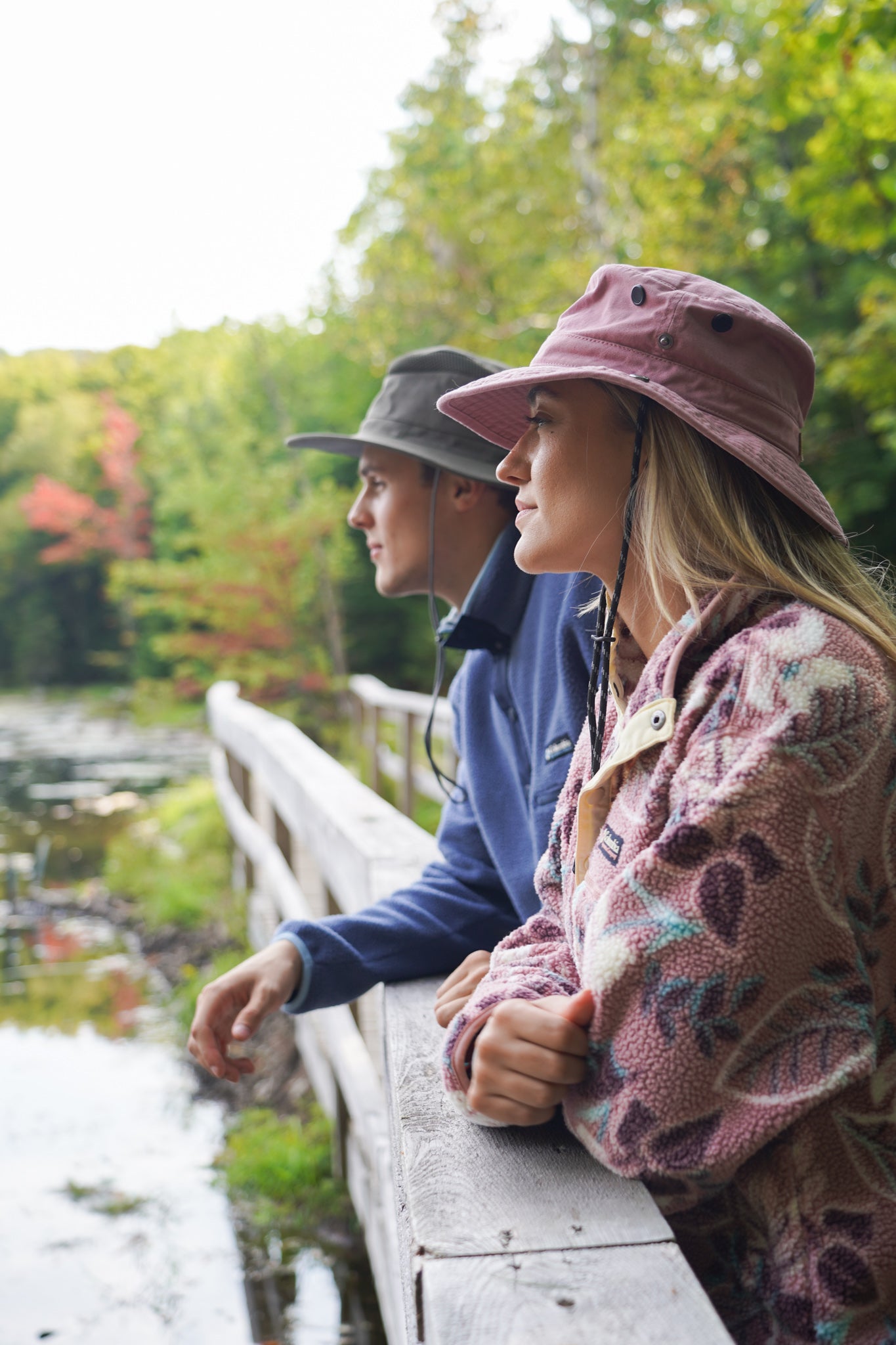 Two people standing on a wooden bridge over a stream with trees in the background