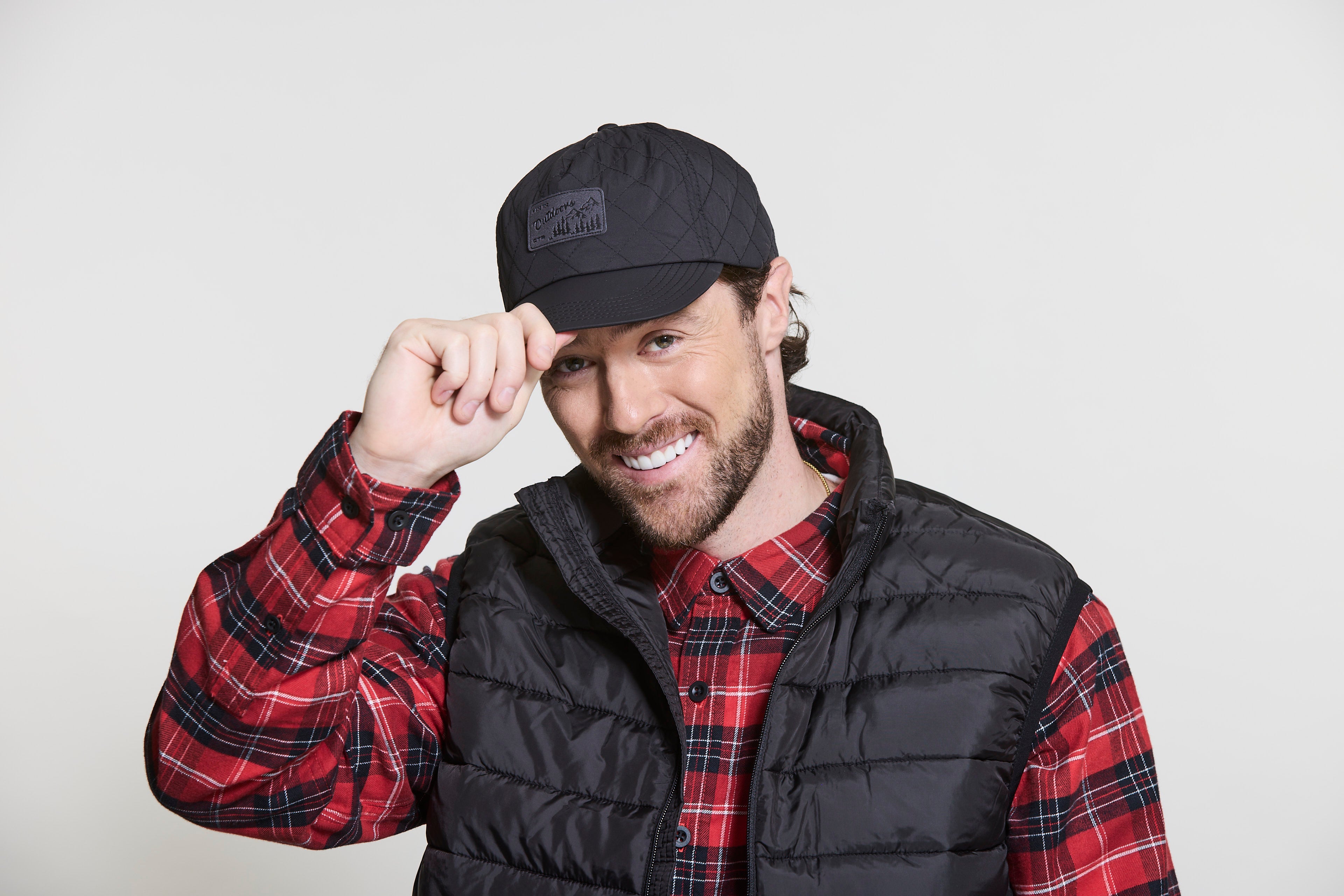 Man wearing a black CTR Outdoors cap, black puffer vest, and red plaid shirt against a white background